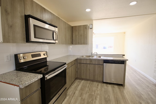 kitchen featuring sink, light stone counters, light wood-type flooring, appliances with stainless steel finishes, and decorative backsplash