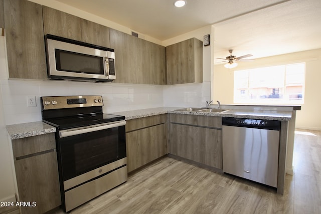 kitchen featuring sink, light stone counters, light hardwood / wood-style flooring, appliances with stainless steel finishes, and backsplash