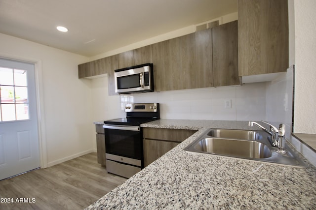 kitchen featuring sink, tasteful backsplash, light stone counters, light hardwood / wood-style flooring, and stainless steel appliances