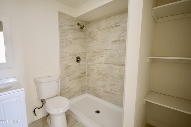 bathroom featuring vanity, a tile shower, and toilet