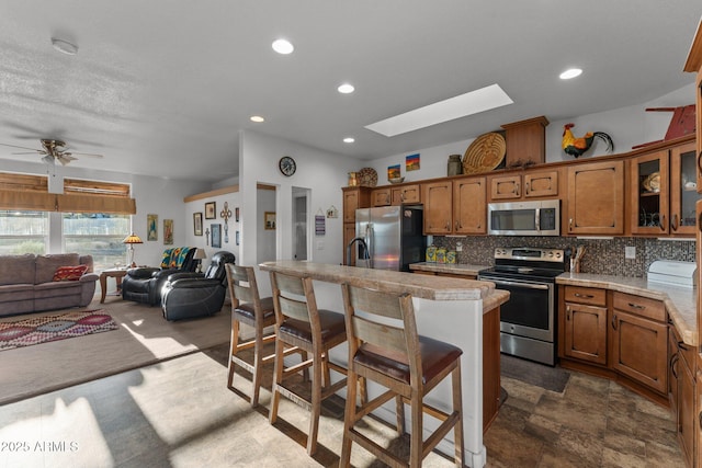 3874 Pura Vida Trl, Wickenburg, AZ 85390 - kitchen with open floor plan, tasteful backsplash, stainless steel appliances, a skylight, and brown cabinetry