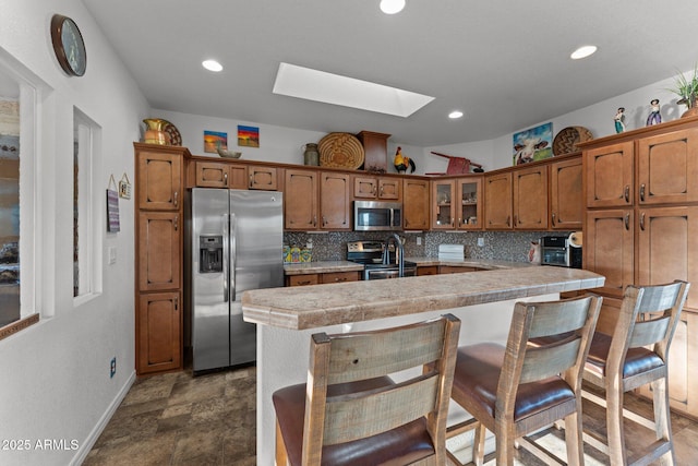 3874 Pura Vida Trl, Wickenburg, AZ 85390 - kitchen featuring light countertops, backsplash, a skylight, appliances with stainless steel finishes, and brown cabinets