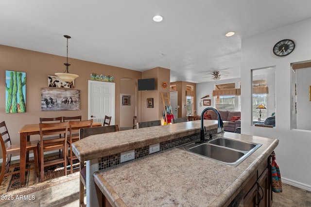 3874 Pura Vida Trl, Wickenburg, AZ 85390 - kitchen with light countertops, a ceiling fan, a center island with sink, a sink, and pendant lighting