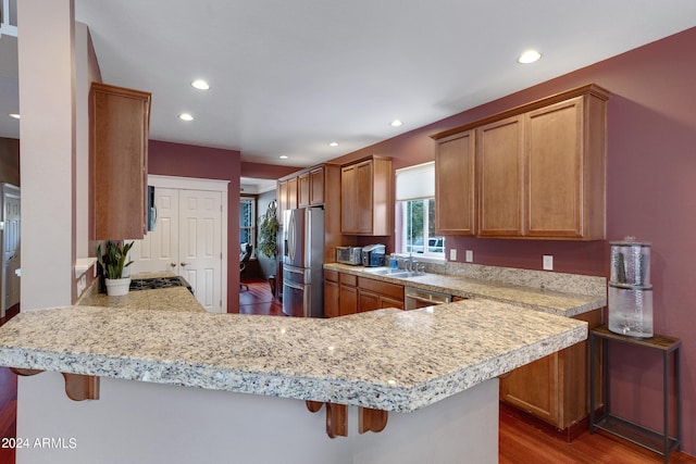 kitchen with hardwood / wood-style floors, a kitchen breakfast bar, sink, kitchen peninsula, and appliances with stainless steel finishes