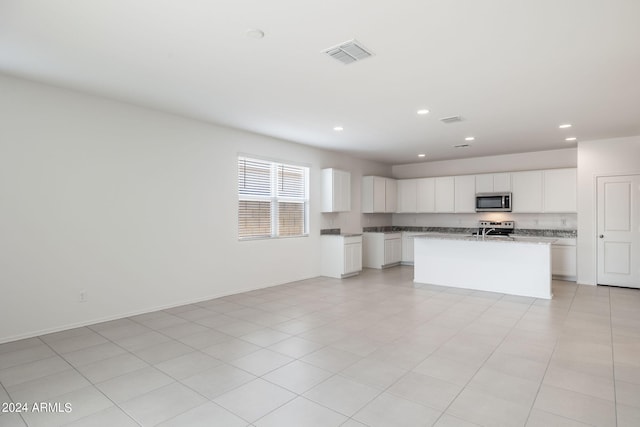 kitchen with appliances with stainless steel finishes, light stone counters, a kitchen island with sink, light tile patterned floors, and white cabinetry