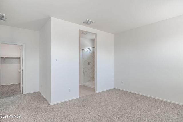 unfurnished bedroom featuring connected bathroom, a walk in closet, a closet, and light carpet