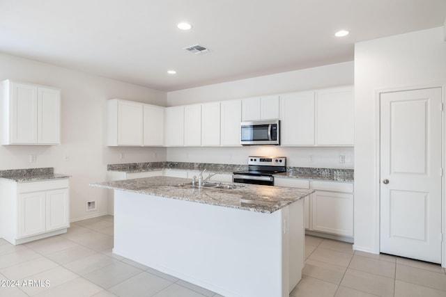 kitchen with light stone countertops, stainless steel appliances, a kitchen island with sink, light tile patterned floors, and white cabinetry