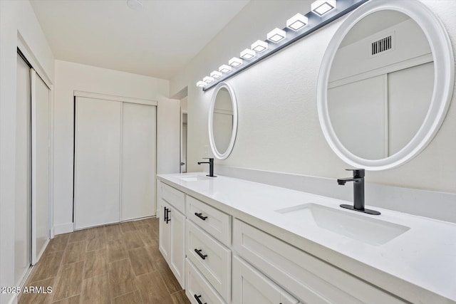 bathroom with double vanity, wood finish floors, a sink, and visible vents