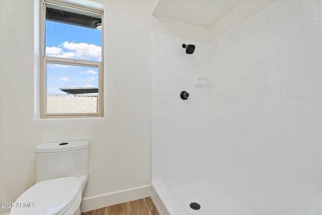 bathroom with a tile shower, wood finished floors, toilet, and baseboards