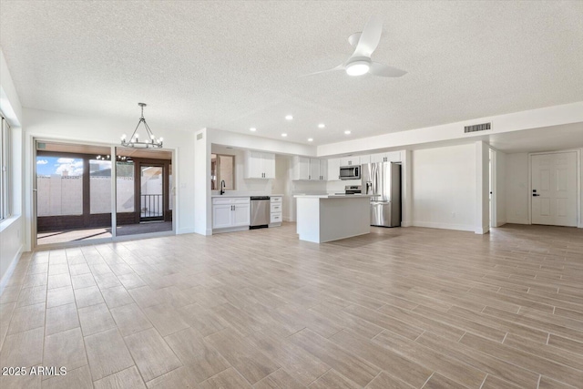 unfurnished living room with visible vents, a textured ceiling, wood finish floors, a sink, and ceiling fan with notable chandelier