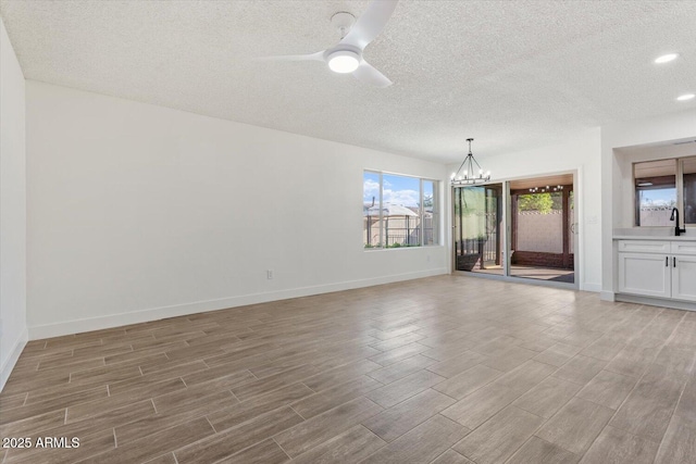 unfurnished room featuring baseboards, wood tiled floor, a textured ceiling, a sink, and ceiling fan with notable chandelier