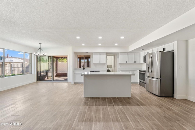 kitchen featuring white cabinetry, light countertops, appliances with stainless steel finishes, light wood finished floors, and an inviting chandelier