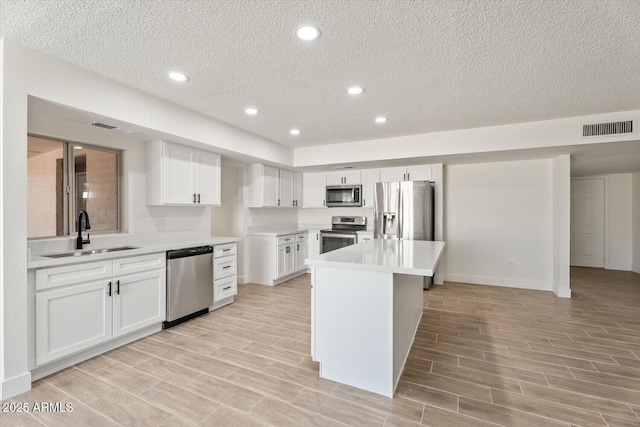 kitchen featuring a center island, stainless steel appliances, visible vents, white cabinetry, and a sink