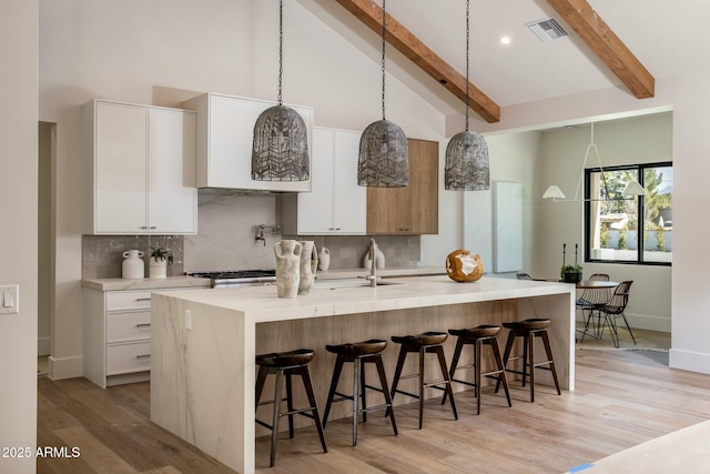 kitchen featuring hanging light fixtures, a kitchen breakfast bar, white cabinets, a center island with sink, and beamed ceiling