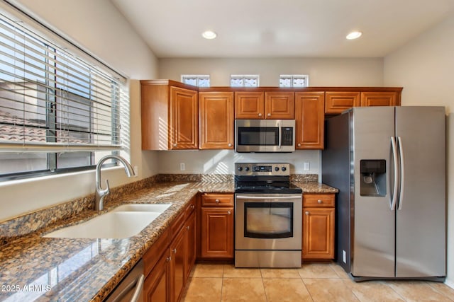 kitchen with stainless steel appliances, stone countertops, brown cabinetry, and a sink