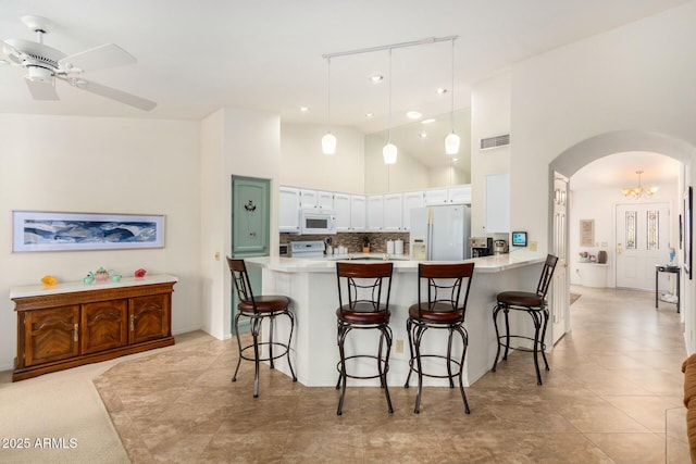 kitchen with white appliances, high vaulted ceiling, a kitchen breakfast bar, kitchen peninsula, and white cabinetry