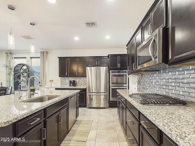 kitchen with dark brown cabinetry, sink, decorative light fixtures, appliances with stainless steel finishes, and light stone countertops