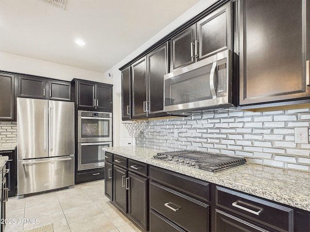 kitchen with backsplash, appliances with stainless steel finishes, light stone counters, and light tile patterned floors