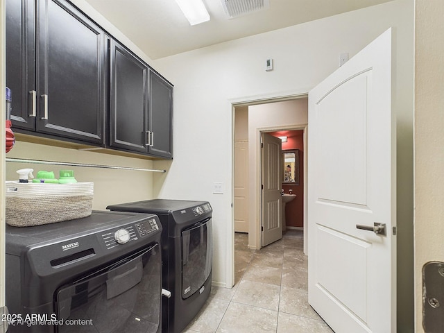 clothes washing area with light tile patterned floors, washer and clothes dryer, and cabinets