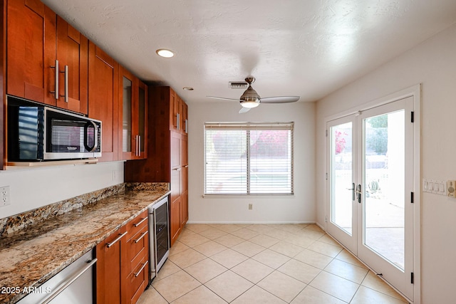 kitchen featuring beverage cooler, glass insert cabinets, brown cabinetry, and light stone countertops