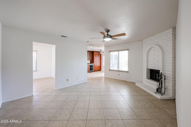 unfurnished living room featuring light tile patterned floors, baseboards, visible vents, ceiling fan, and a brick fireplace