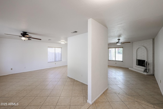 unfurnished room featuring visible vents, a ceiling fan, light tile patterned floors, baseboards, and a brick fireplace