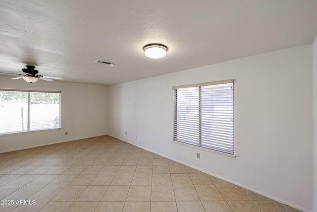 empty room with light tile patterned floors, visible vents, a textured ceiling, and a ceiling fan