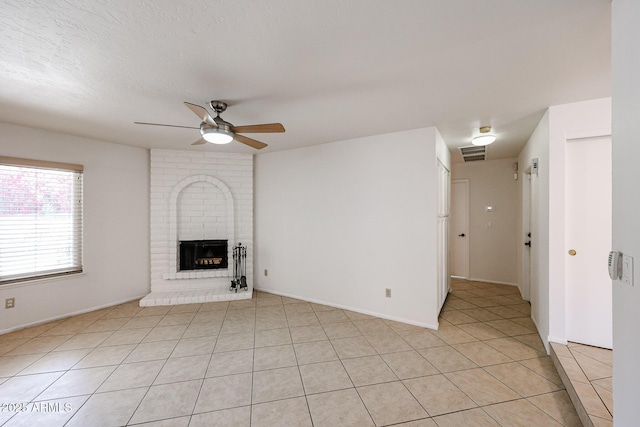 unfurnished living room featuring visible vents, a ceiling fan, a textured ceiling, light tile patterned floors, and a brick fireplace