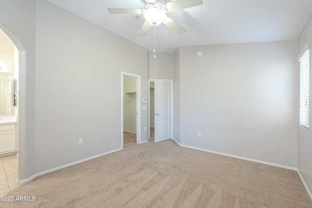 unfurnished bedroom with connected bathroom, ceiling fan, a walk in closet, light carpet, and a closet