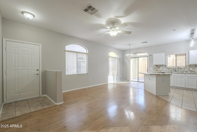 kitchen with backsplash, ceiling fan with notable chandelier, pendant lighting, white cabinets, and a center island