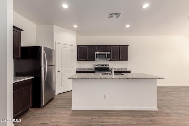 kitchen featuring light stone countertops, appliances with stainless steel finishes, a kitchen island with sink, and sink