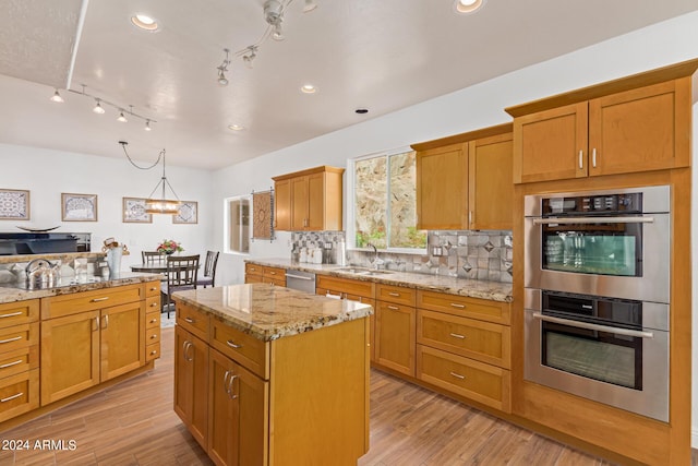 kitchen with sink, a center island, stainless steel appliances, light hardwood / wood-style floors, and backsplash