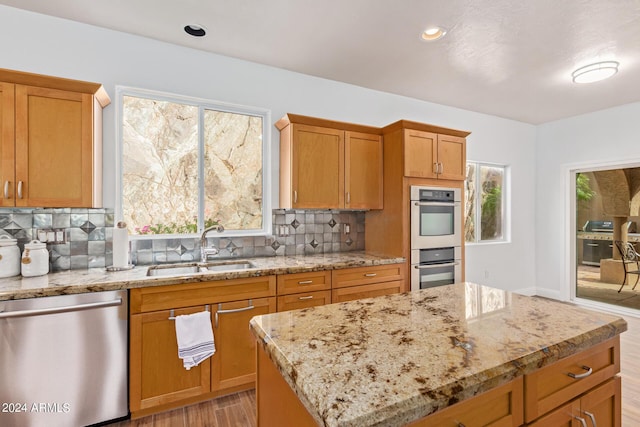 kitchen with sink, stainless steel appliances, light stone counters, a kitchen island, and decorative backsplash