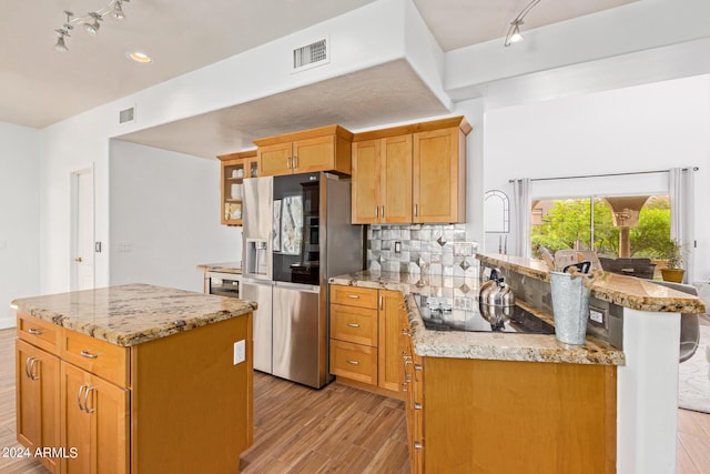 kitchen with light hardwood / wood-style flooring, a center island, stainless steel refrigerator with ice dispenser, black electric stovetop, and decorative backsplash