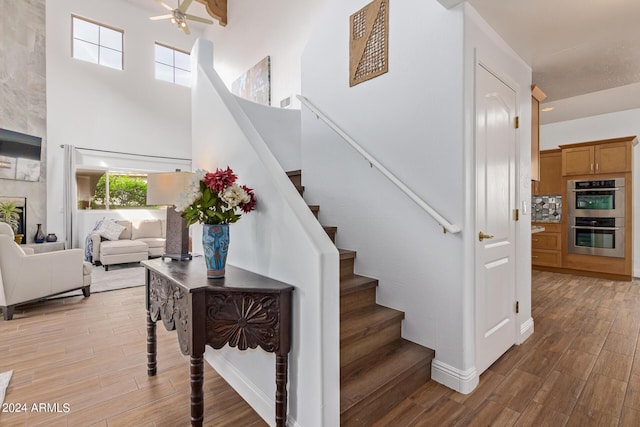 stairway with a high ceiling, hardwood / wood-style floors, and ceiling fan