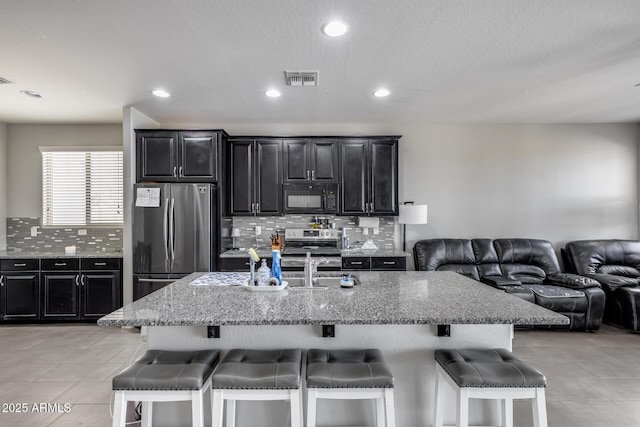 kitchen with dark cabinets, decorative backsplash, a breakfast bar area, stainless steel appliances, and open floor plan