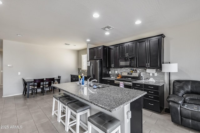 kitchen featuring tasteful backsplash, appliances with stainless steel finishes, dark cabinetry, a sink, and a kitchen breakfast bar