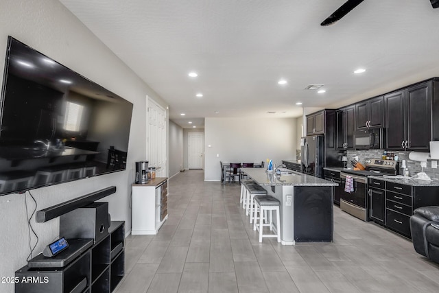 kitchen featuring electric stove, a kitchen island with sink, freestanding refrigerator, black microwave, and a kitchen breakfast bar