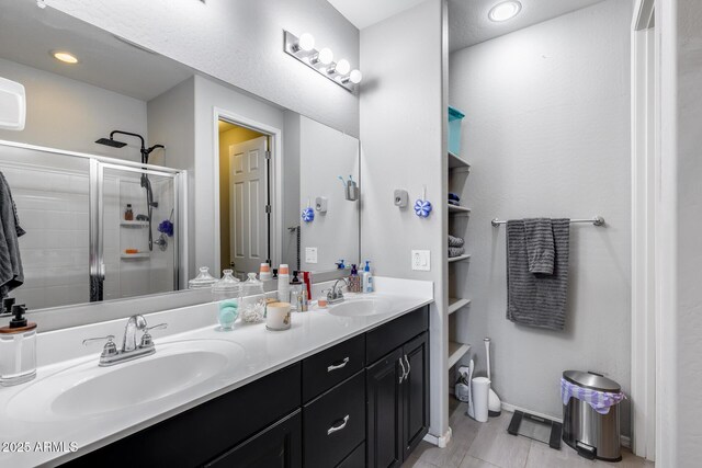 full bathroom with a stall shower, double vanity, and a sink