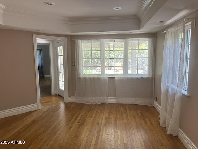 empty room with a tray ceiling, ornamental molding, a healthy amount of sunlight, and light wood-type flooring