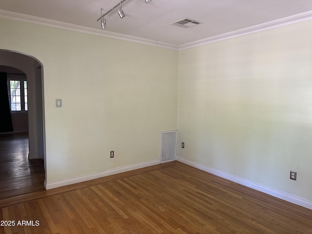 empty room with dark wood-type flooring, track lighting, and ornamental molding