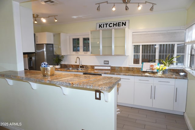 kitchen featuring sink, a breakfast bar area, stainless steel fridge, kitchen peninsula, and white cabinets