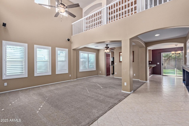 unfurnished living room with ceiling fan with notable chandelier, light tile patterned flooring, and a high ceiling