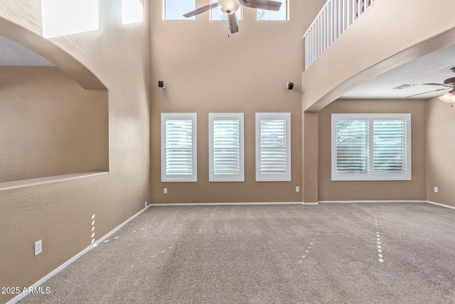 unfurnished living room with ceiling fan, carpet floors, and a high ceiling