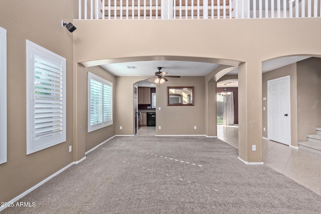 unfurnished living room featuring ceiling fan with notable chandelier, light colored carpet, and a high ceiling