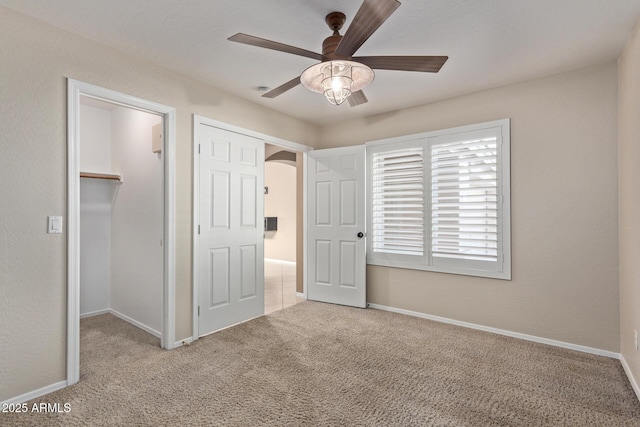 unfurnished bedroom featuring ceiling fan, a spacious closet, light carpet, and a closet