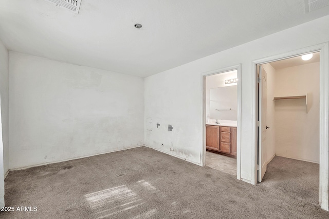 unfurnished bedroom with a walk in closet, light colored carpet, connected bathroom, and visible vents