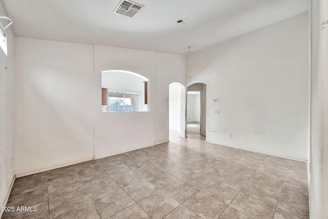 unfurnished room featuring light tile patterned floors, visible vents, and arched walkways