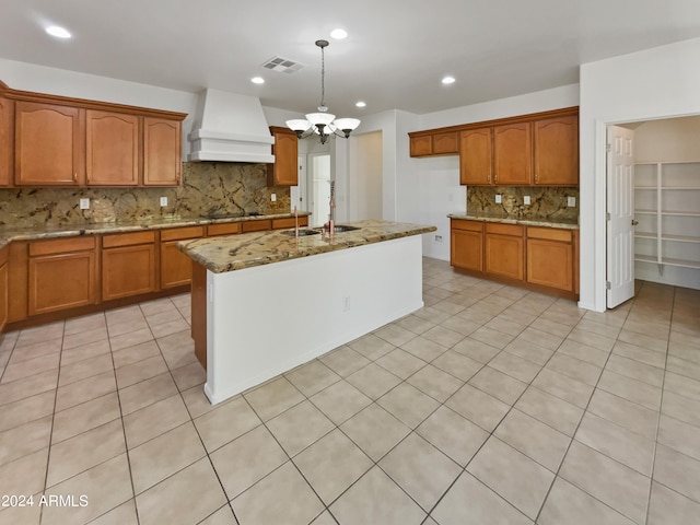 kitchen with light stone counters, sink, a notable chandelier, hanging light fixtures, and custom exhaust hood