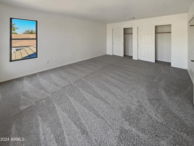 unfurnished bedroom with two closets and dark colored carpet